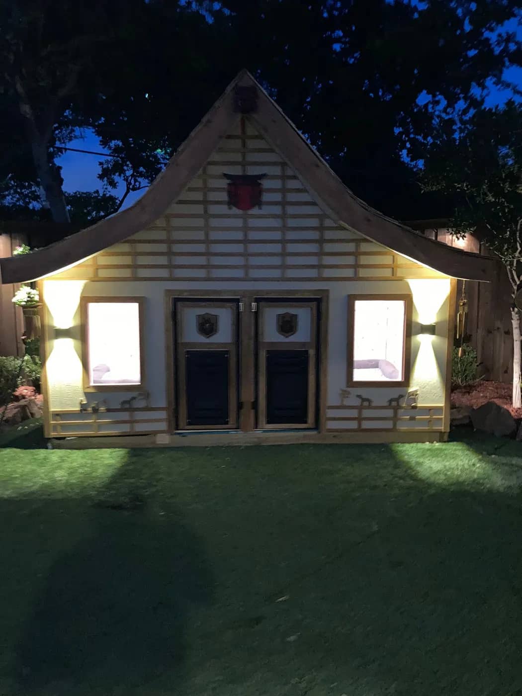 The finished garden playhouse lit from within at dusk