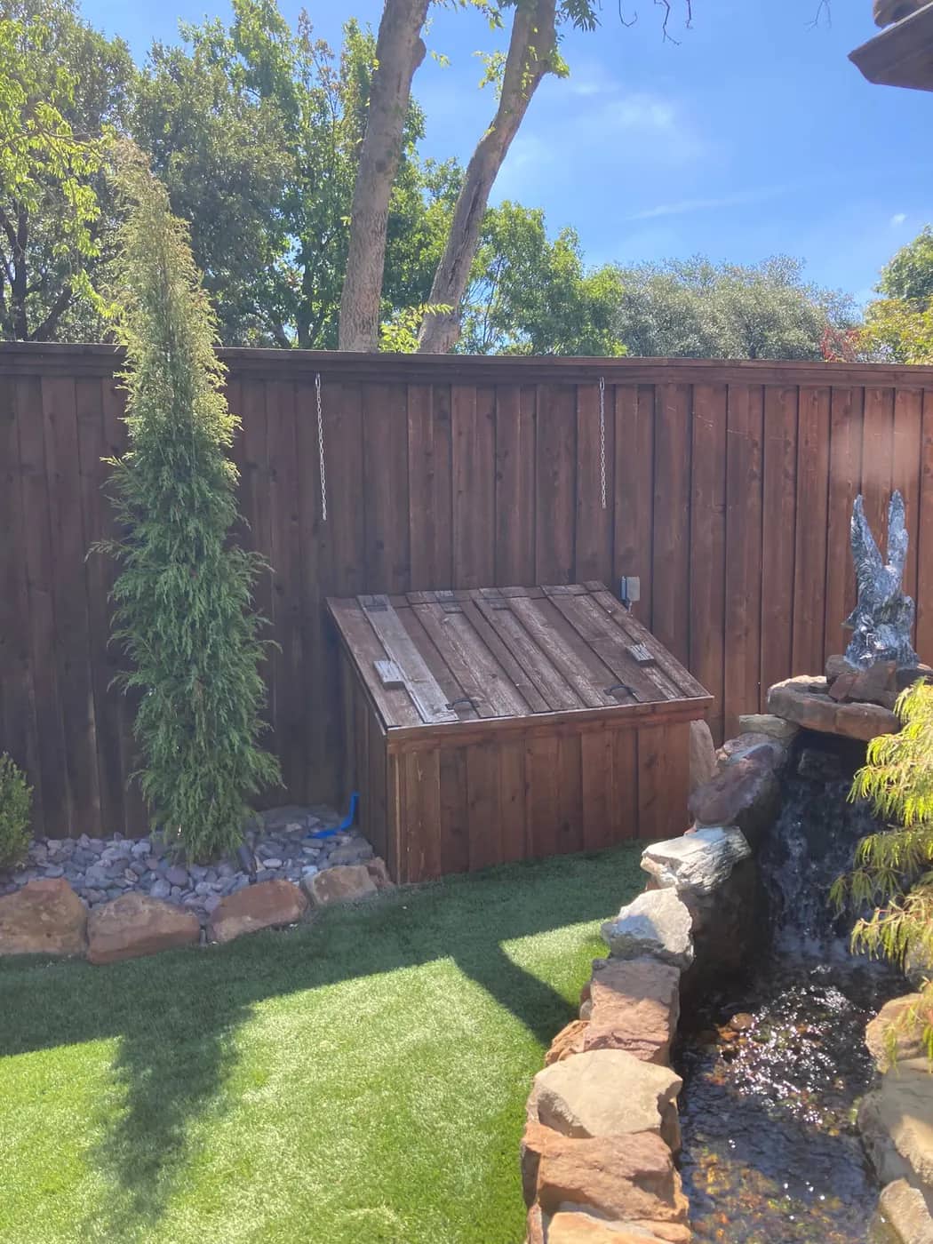 Landscaped garden with a stone water feature, artificial lawn and a low cedar equipment store