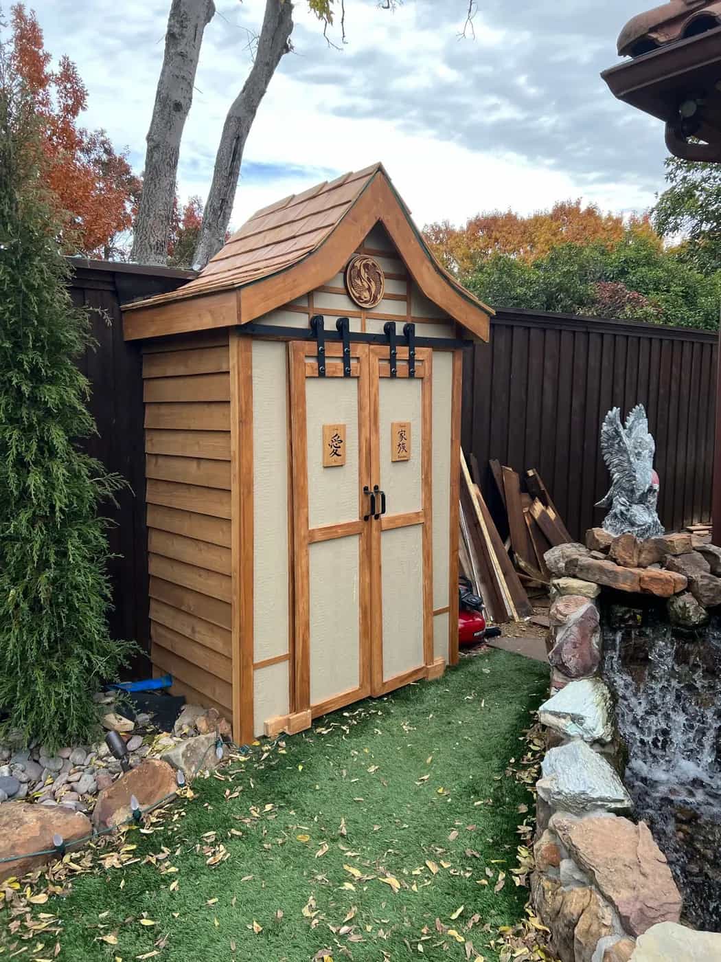 Completed cedar garden store with panelled doors beside a rock water feature