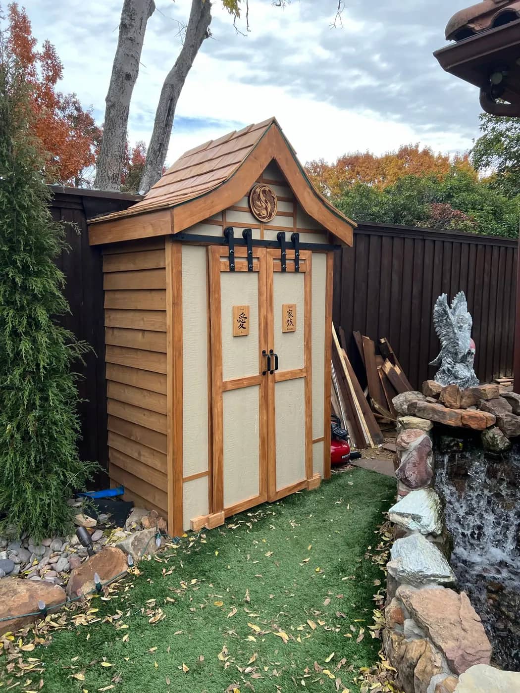 Completed cedar garden store with panelled doors beside a rock water feature